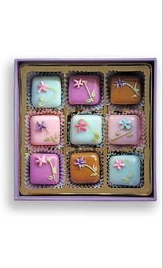 an assortment of decorated chocolates in a purple gift box with pink and blue frosting