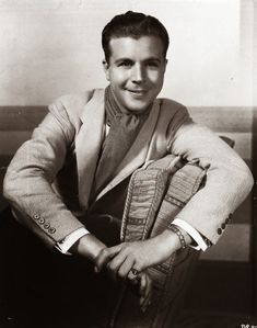 an old photo of a man in a suit and tie sitting on a chair with his arms crossed