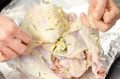 two hands are peeling the skin of a piece of meat on tin foil with herbs and seasoning