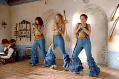 three women in blue and yellow outfits are dancing on the dance floor with their instruments