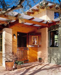 a small house with wood trimmings and wooden doors on the front door is surrounded by greenery