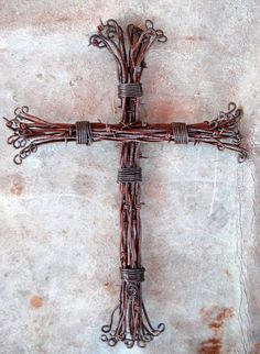 a cross made out of branches on a stone wall with rusted metal wires attached to it