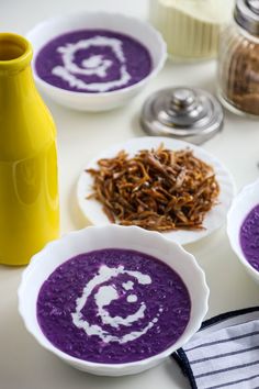 three bowls filled with purple soup next to some spoons and other items on a table