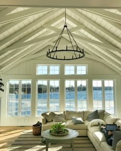 a living room filled with white furniture and windows next to a large body of water