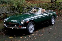 a green convertible car parked on the side of a road next to a stone wall