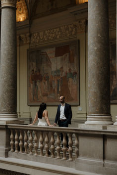 a bride and groom standing on the balcony of an old building with paintings behind them