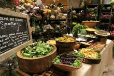 an assortment of fresh vegetables on display at a market stall with chalkboard sign in the background