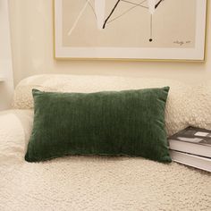 a green pillow sitting on top of a white bed next to a book and lamp