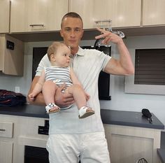 a man holding a baby in his arms and pointing at the camera with both hands