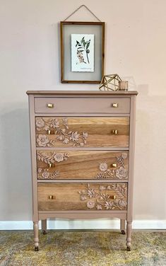 a pink dresser with flowers on it and a framed picture above the drawers in an empty room