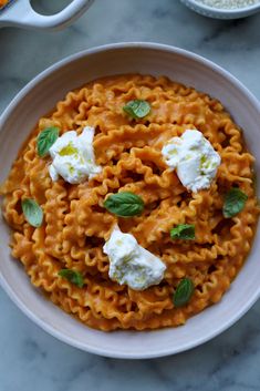 a white bowl filled with pasta and topped with whipped cream on top of a marble table