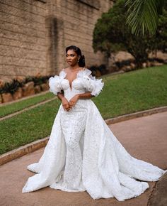 a woman in a white wedding dress standing on the sidewalk with her arms crossed and looking off to the side