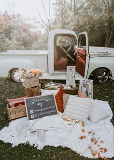 an old white truck parked on top of a grass covered field next to a pile of blankets