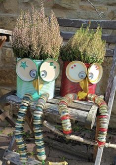 two owls made out of tin cans sitting on a bench with flowers in the back