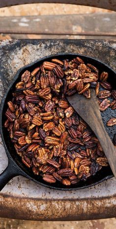 pecans frying in a cast iron skillet with a wooden spoon on the side