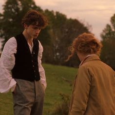 two people standing next to each other in front of a field with trees and grass