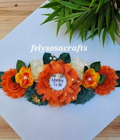 an orange and white flower headband with green leaves on the top, reads felyssocrafts mommy to be