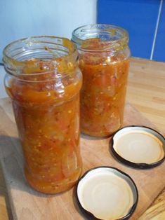 two jars filled with food sitting on top of a wooden cutting board next to plates