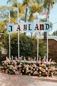 a sign that says jayland with flowers in the foreground and palm trees behind it