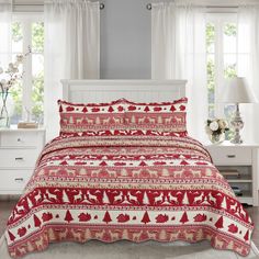 a bed with red and white bedspread in front of two windows next to a night stand