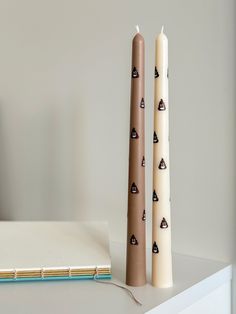 two candles sitting next to each other on top of a white table with a notebook