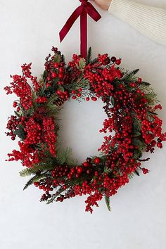 a hand holding a christmas wreath with red berries and greenery