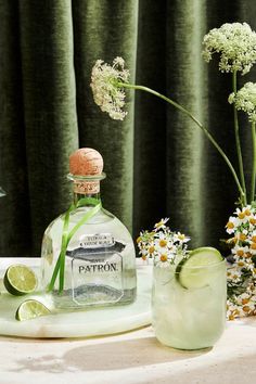 a bottle of patron gin on a table with flowers and limes in the background