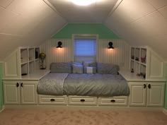 a bed sitting in the middle of a bedroom under a slanted ceiling with built - in bookshelves