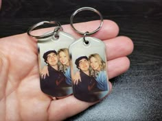 a person holding two keychains in their left hand, with the image of two women on them