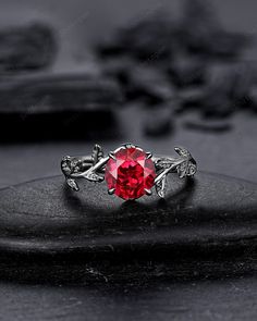 a red ring sitting on top of a black stone slab with leaves and vines around it