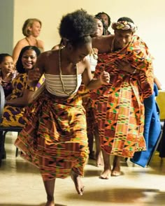 two women in colorful dresses dancing with other people behind them and one woman standing on the floor