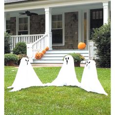 three white ghost statues in front of a house with pumpkins on the porch and lawn