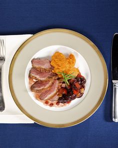 a white plate topped with meat next to a fork and knife