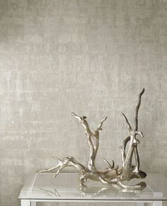 a silver vase with branches in it sitting on a glass table next to a wall