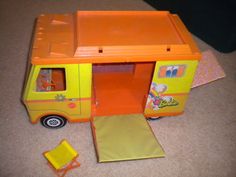 an orange and yellow toy truck with its door open on the floor next to a chair