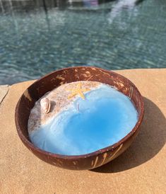 a bowl filled with blue liquid sitting on top of a table next to a swimming pool