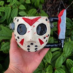 a hand holding a toy mask with two knives in it's mouth and the face painted red