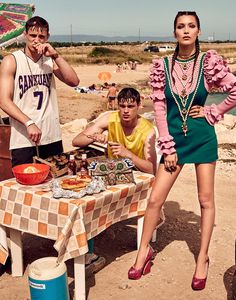 three people standing around a table with food on it and an umbrella in the background