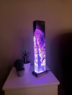 a purple lamp sitting on top of a white table next to a potted plant