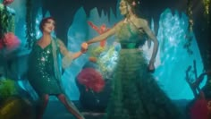 two women dressed in green dresses are dancing with their hands together and one is holding the other's hand