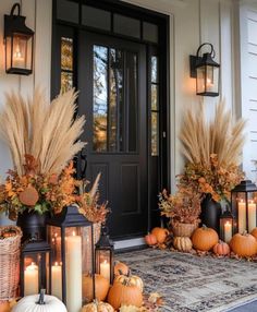 a front porch decorated for fall with pumpkins, wheat stalks and candles on the doorstep