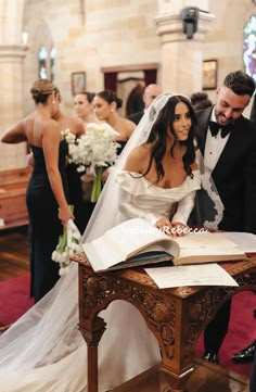 a bride and groom signing the register at their wedding ceremony in an old church with other people looking on