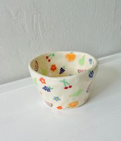 a white bowl with fruit designs on it sitting on top of a counter next to a wall