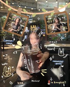 a woman holding a drink in front of her face and photos on the wall behind her