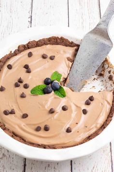 a pie with chocolate and mints on top in a white bowl next to a knife