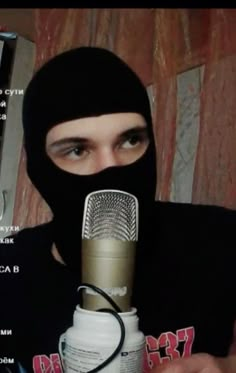 a person wearing a black head covering holding a microphone in front of their face with the caption on it