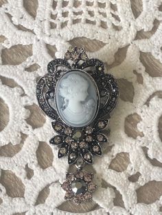 A two tone Gray Cameo is lovely in this marcasite-like setting with crystals and a crystal drop. This is a faux cameo brooch but it looks very vintage on a blouse, dress, coat, and sweater. You will surely receive many compliments. This cameo will be sent in a gift box.  If you want this complementary wrapped, please make a note of such in the comments section. All shipments are combined to save on postage costs.  Please email seller if you have any questions. We use USPS First Class Mail and if you need Signature Confirmation pls make a note in the Comments section and add USPS fee of $3.45. Thank you for looking at this Etsy.com shop. Silver Victorian Pins, Groom Lapel Pin, Farmhouse Floral Decor, Hot Air Balloon Centerpieces, Long Beach Ny, Fall Mason Jars, Silver Brooch Pin, Starfish Pendant, Balloon Centerpieces