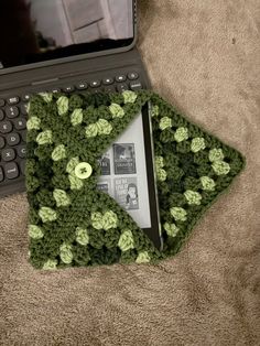 an open laptop computer sitting on top of a bed next to a green crocheted cover