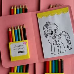 some colored pencils are laying next to each other on pink paper and there is a coloring book with an image of a pony