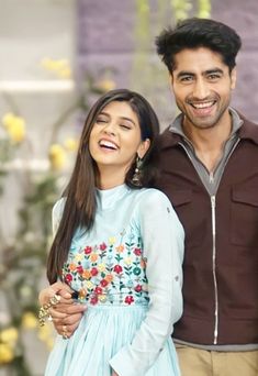 a man and woman standing next to each other in front of a flower filled wall